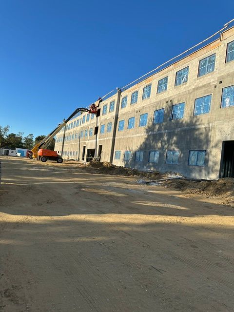 Orange excavator by a long beige building under a clear blue sky