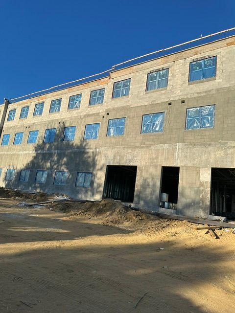 Sunlit unfinished concrete building with blue-tinted windows and open doorways on a dirt lot