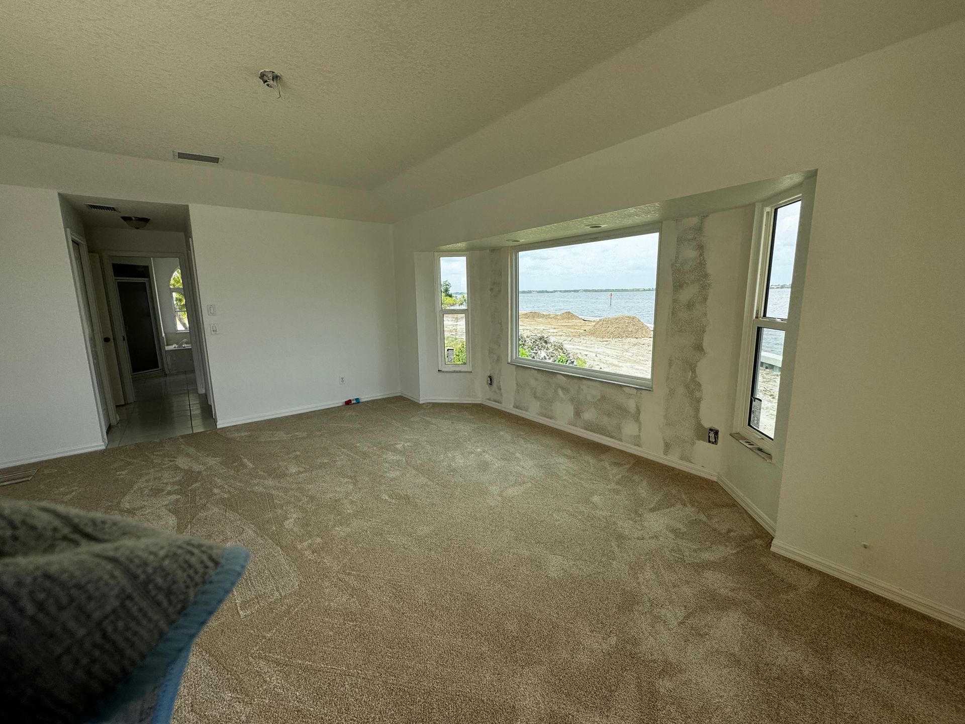 Empty beige-carpeted living room with large bay window and doorway to hall