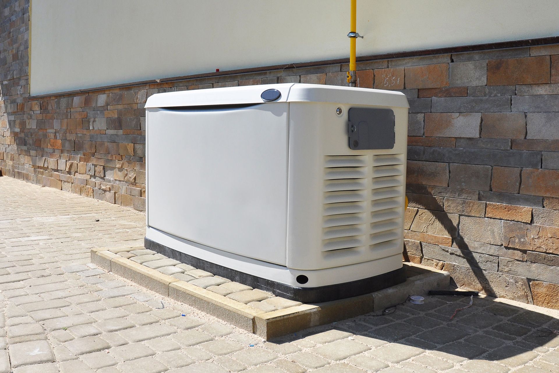 A white generator is sitting on the sidewalk next to a brick wall.