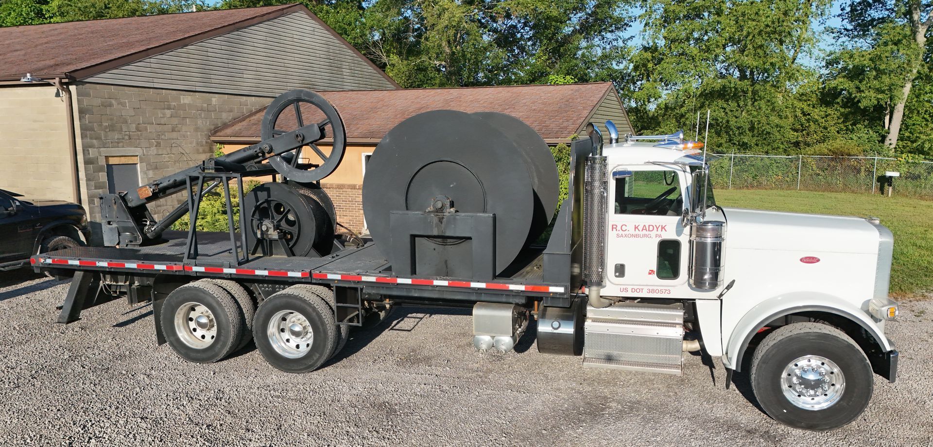 A white semi truck is carrying a large black object on its flatbed.