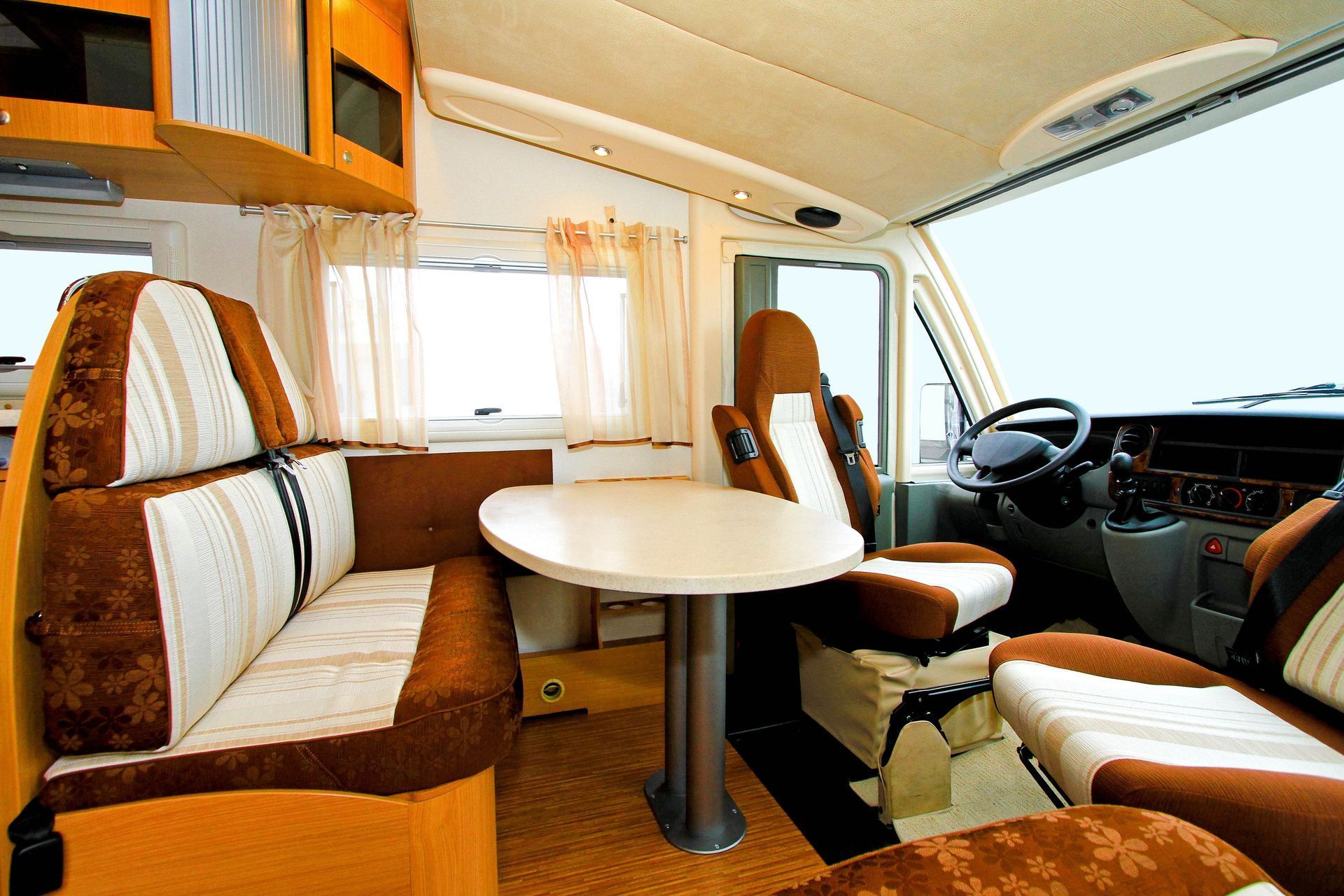 Interior of a motorhome; brown and beige seating, table, steering wheel, and front seats visible.