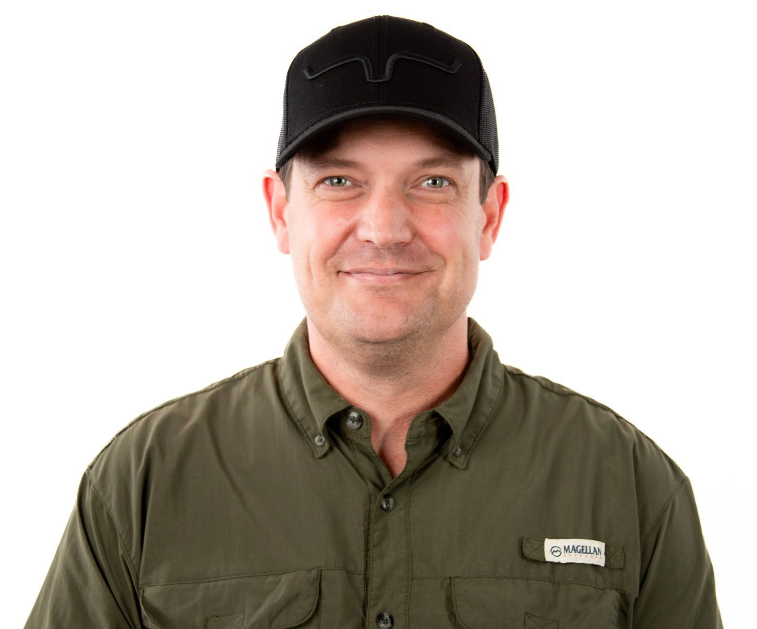 Man in green shirt and black cap smiles, isolated on white background.