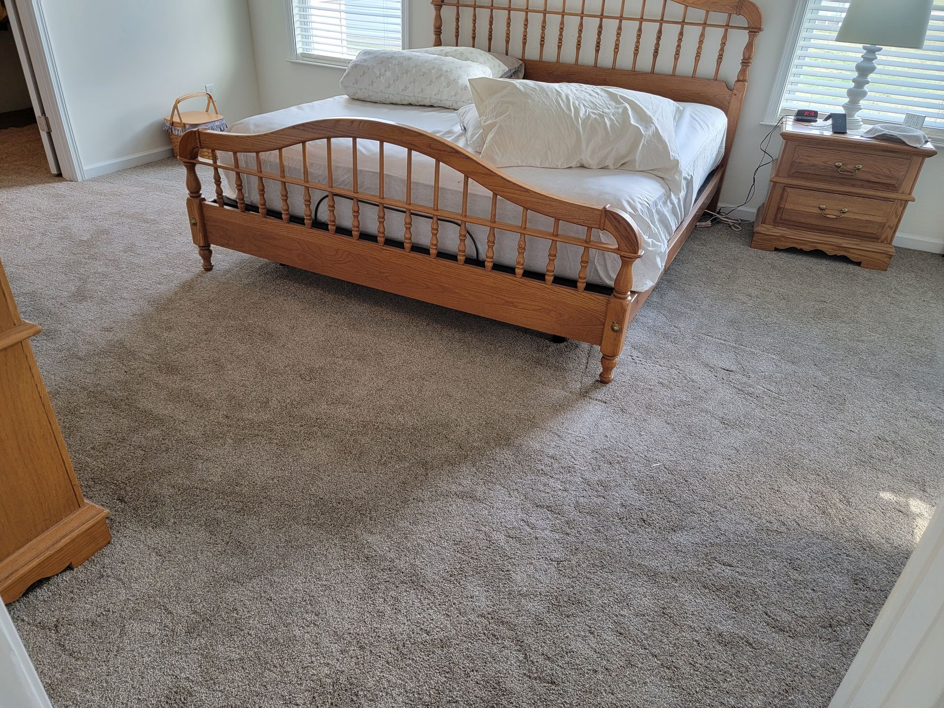 A bedroom with a bed , nightstand , lamp and carpet.
