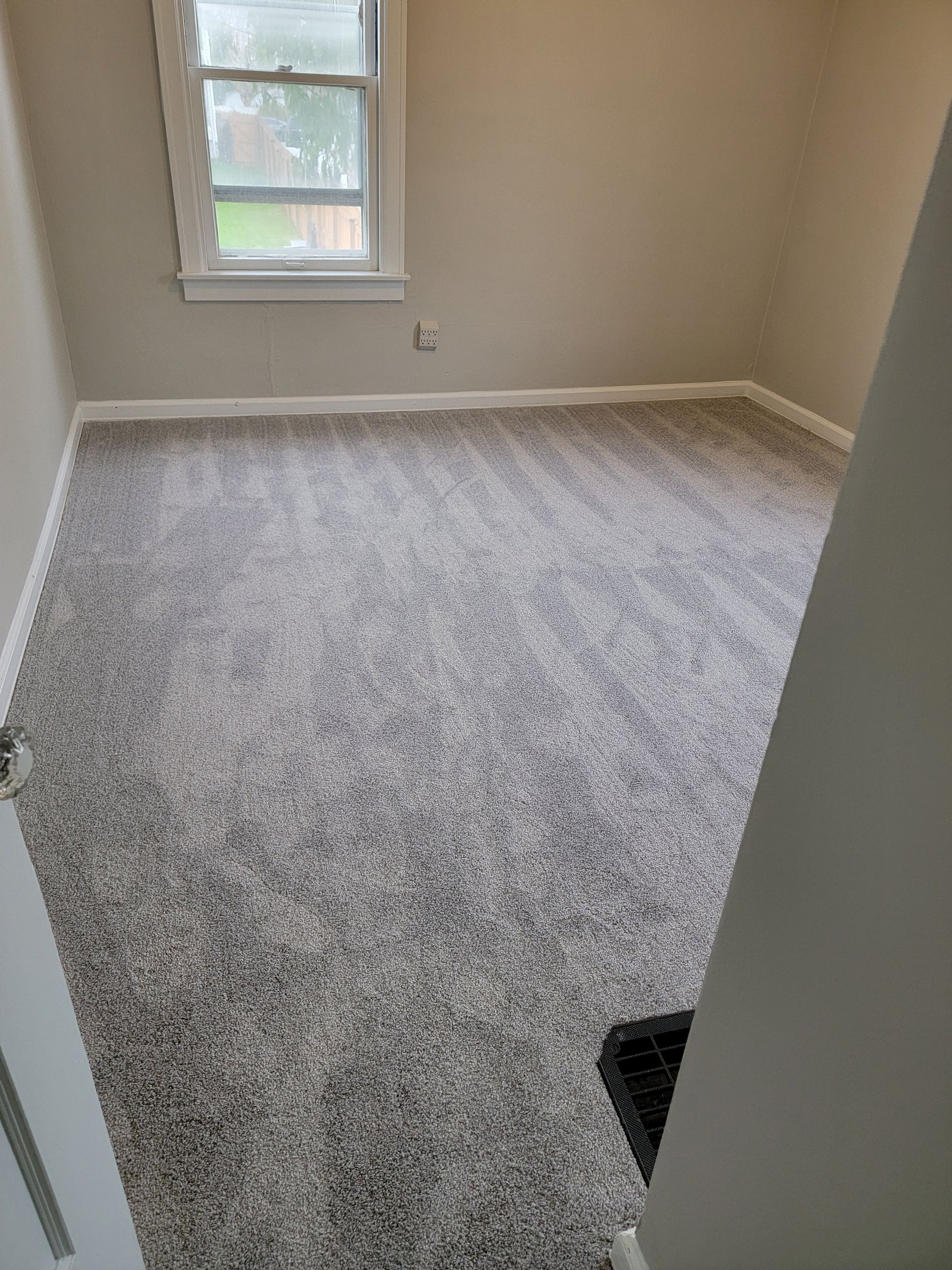 An empty room with a gray carpet and a window.