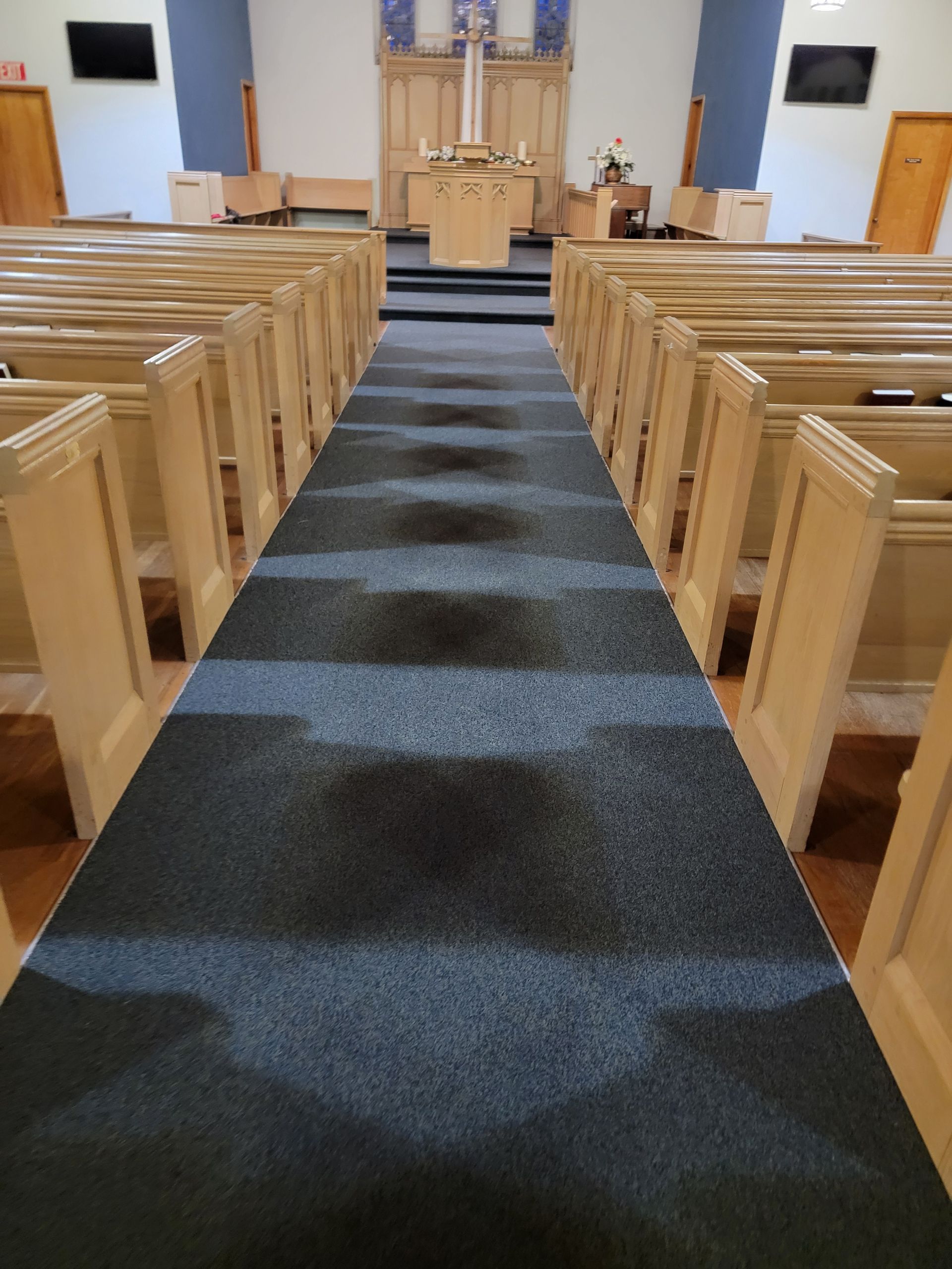 A church with rows of wooden benches and a black carpet leading to the altar.
