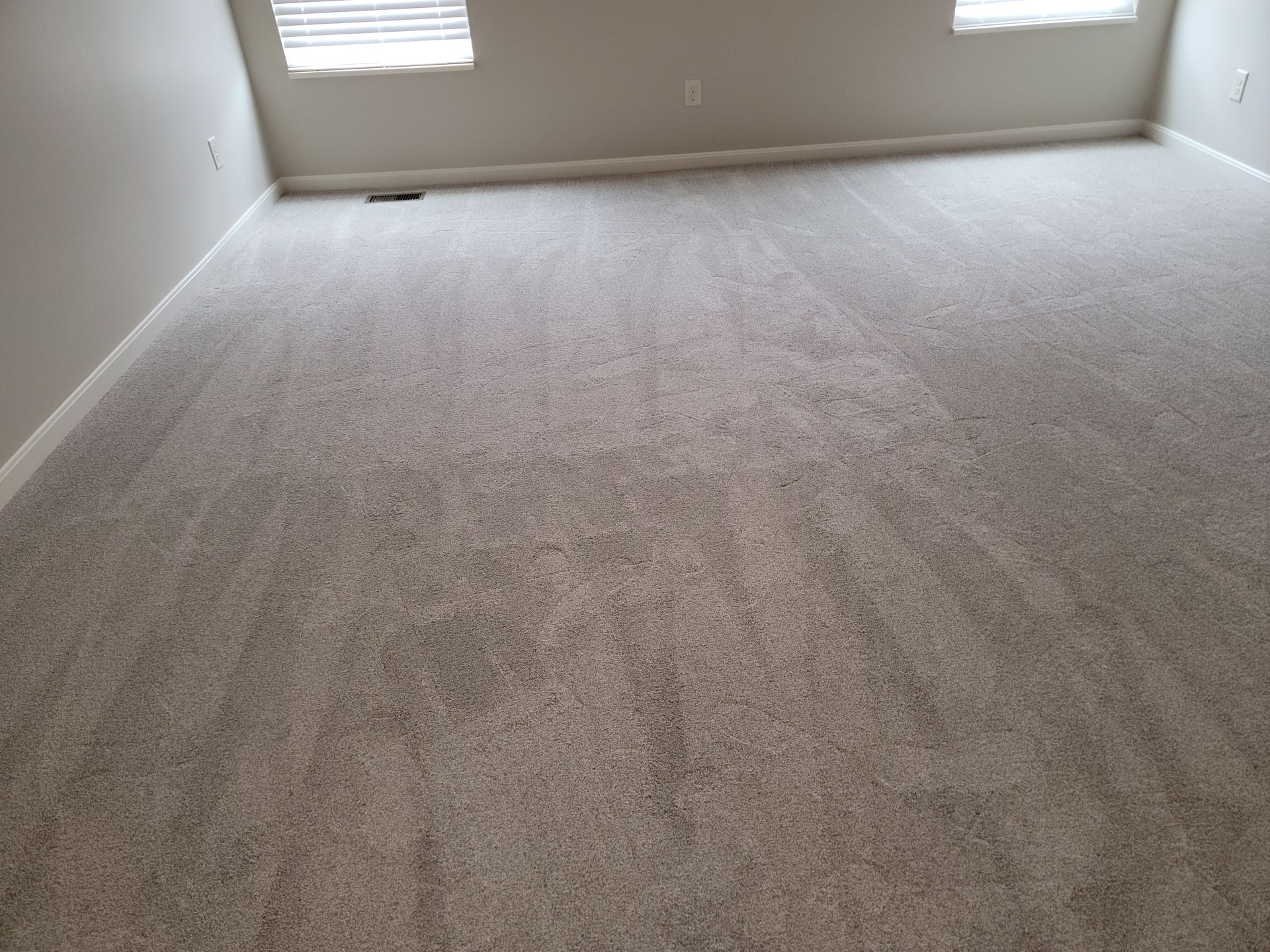 A living room with a large carpeted floor and two windows.