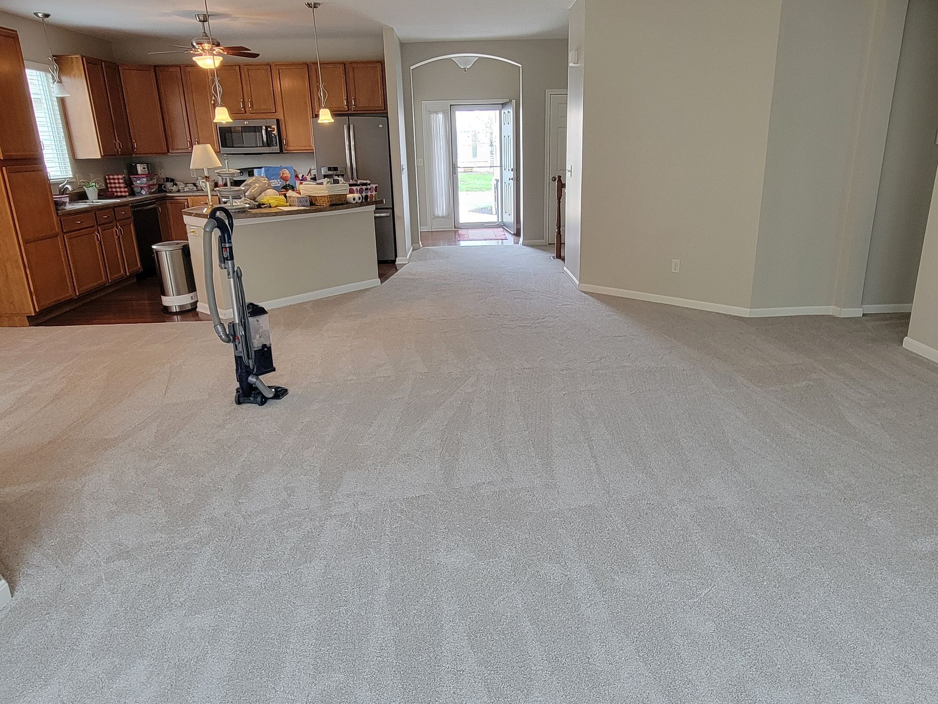 A vacuum cleaner is sitting in a living room next to a kitchen.