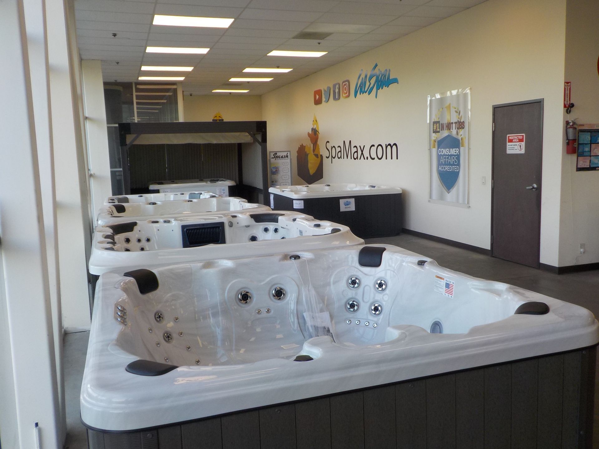 A showroom displaying multiple white hot tubs in a row with white walls and overhead lighting.