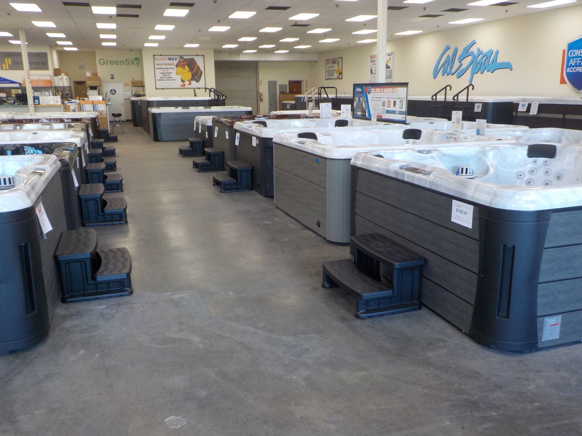 Rows of various hot tubs and spas with stairs on display in a retail showroom.
