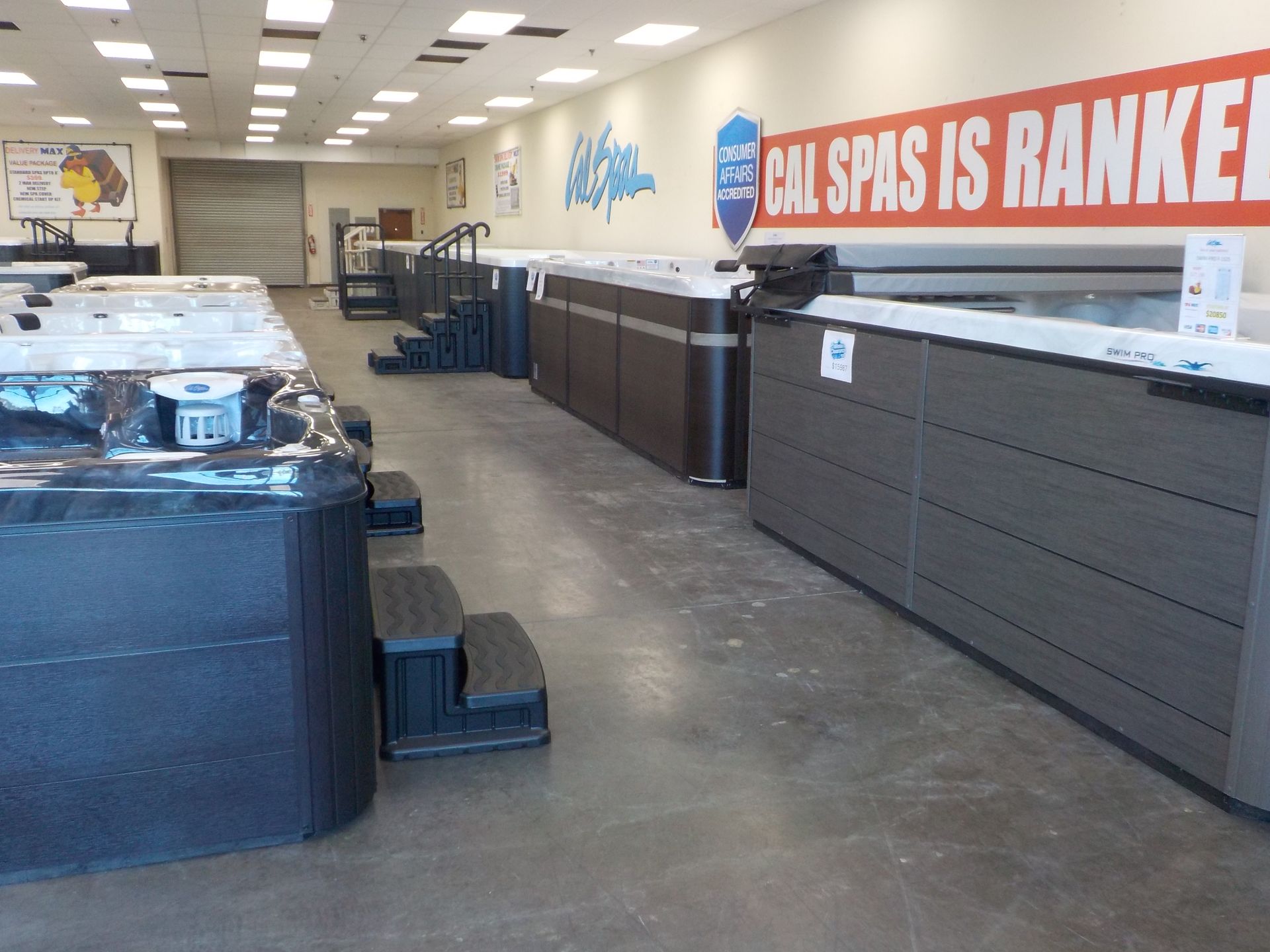 A showroom floor displaying rows of large, rectangular hot tubs in various dark colors, with a branded wall sign.