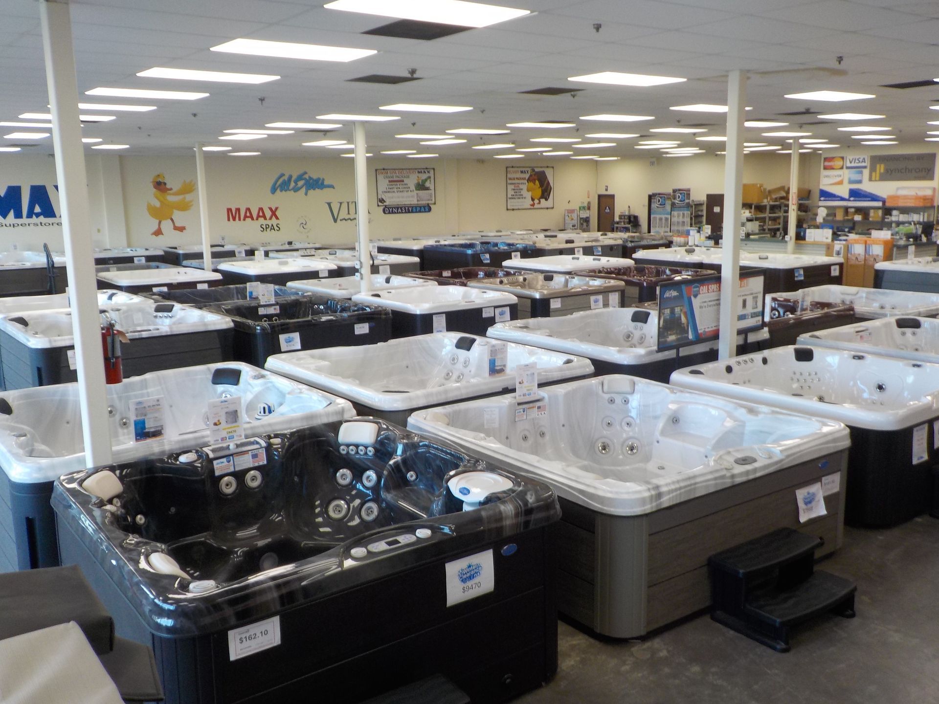 A showroom filled with various hot tubs in a brightly lit indoor space with white walls and a drop ceiling.