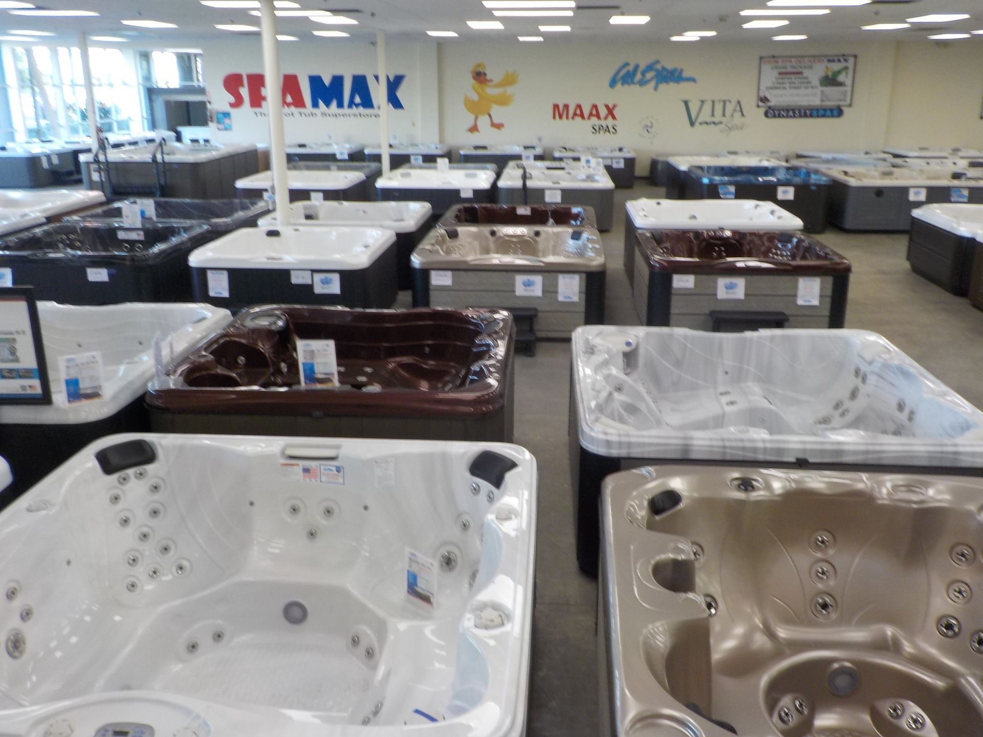 A showroom display features many hot tubs in various colors and sizes, with brand logos visible on the back wall.
