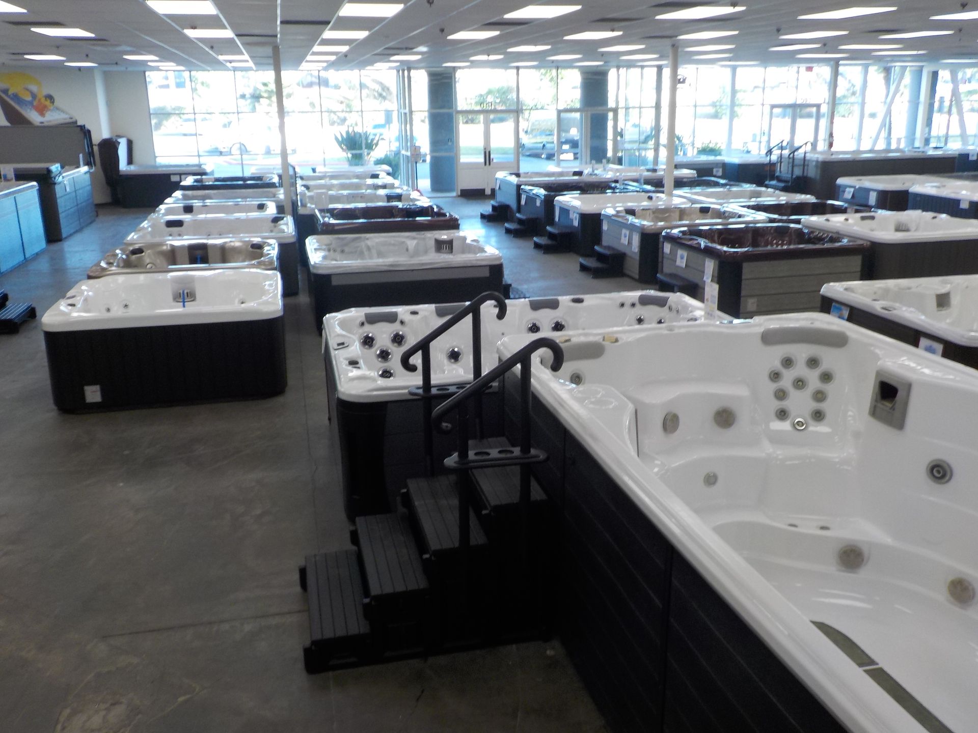 A showroom floor filled with rows of various white and dark-colored hot tubs and spas.