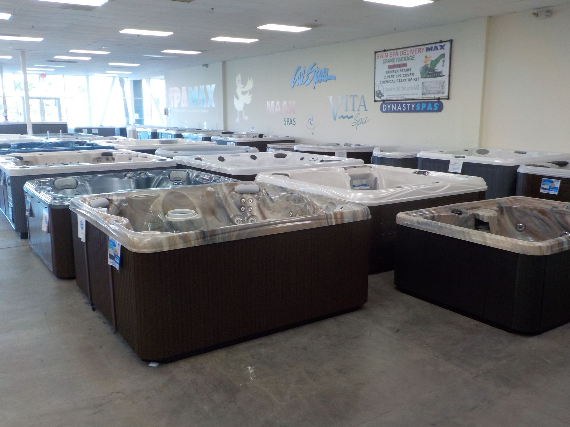 A showroom floor filled with multiple brown and grey hot tubs arranged in rows under bright overhead lighting.