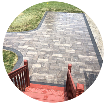 Brick patio with dark edging, red stairs, and green grass.