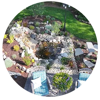 A backyard with a pond, landscaping, chairs, and a lamp post.