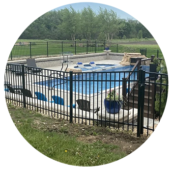 Black fenced-in rectangular pool with blue water, surrounded by a grassy area and trees.