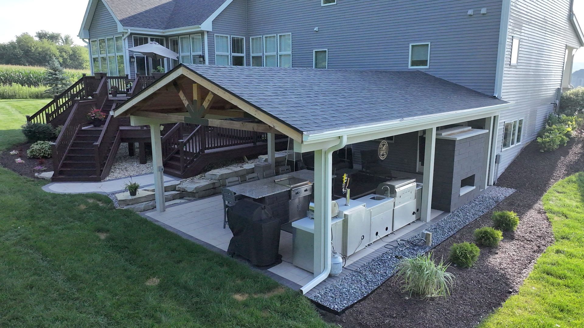 Outdoor kitchen with gray cabinets, a grill, and a roof, attached to a gray house.