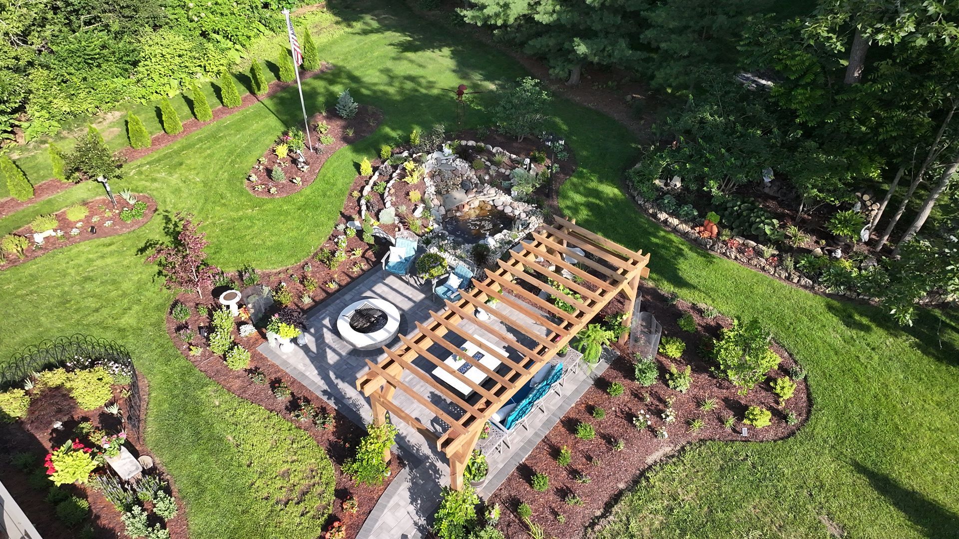 Aerial view of a landscaped backyard with a wooden pergola, fire pit, and garden beds.