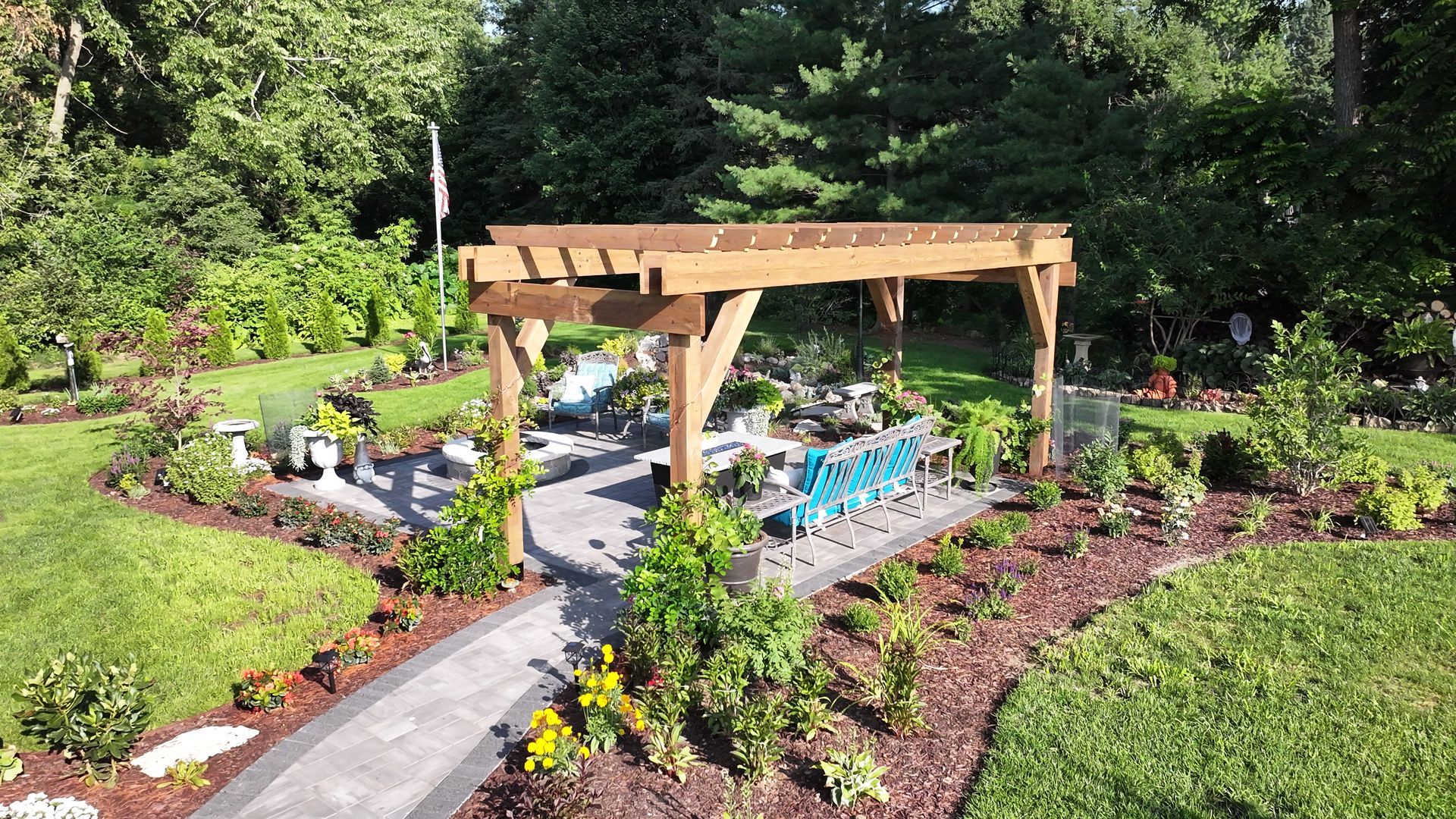 Wooden pergola over a paved path in a garden, surrounded by plants and trees.