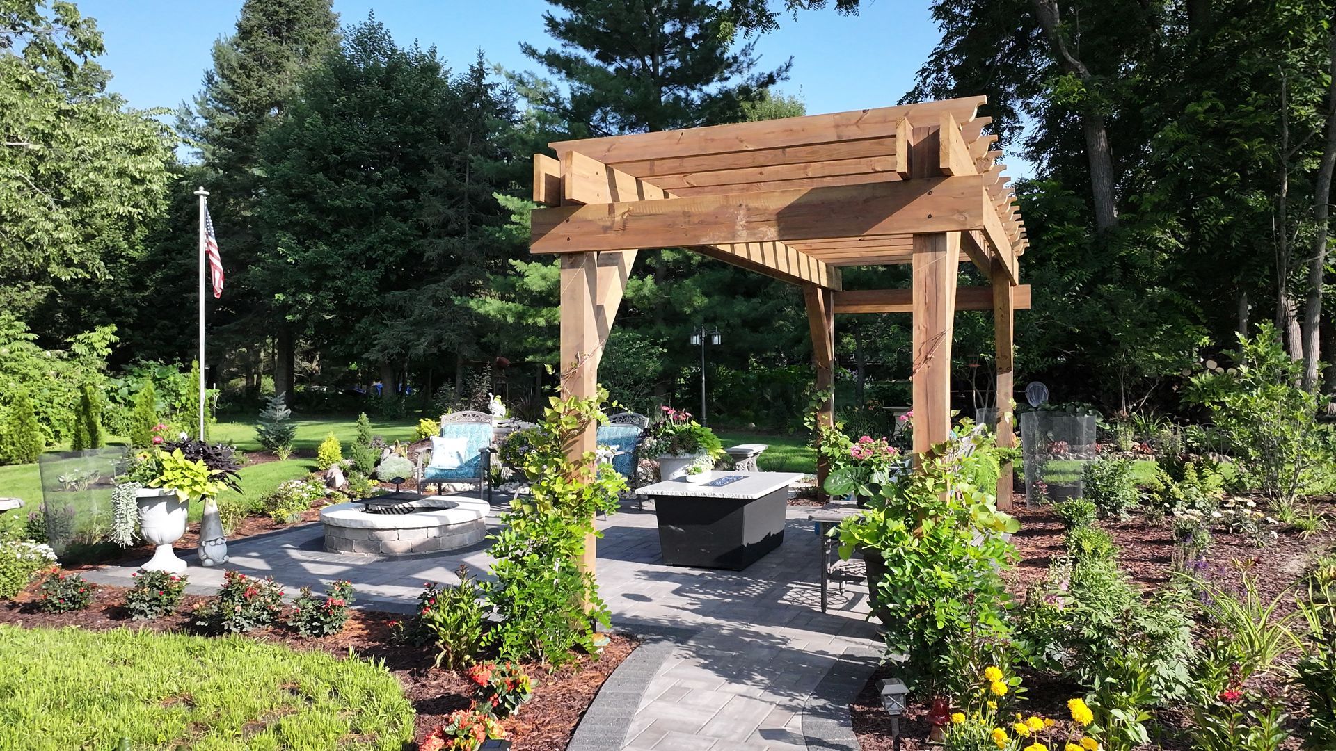 Wooden pergola over patio with seating area, surrounded by garden beds and trees.