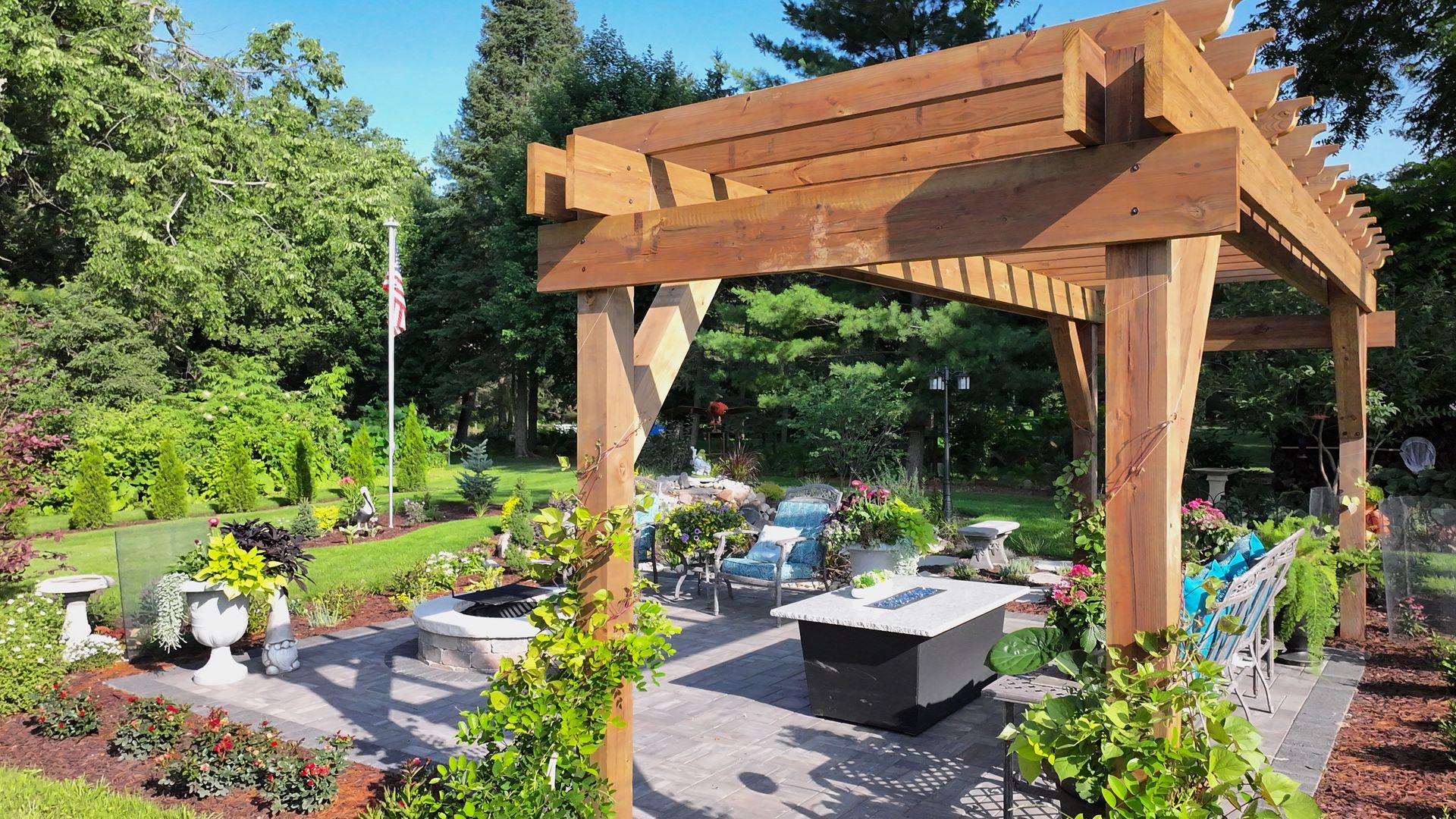 Wooden pergola over a patio with seating, fire pit, and lush garden.