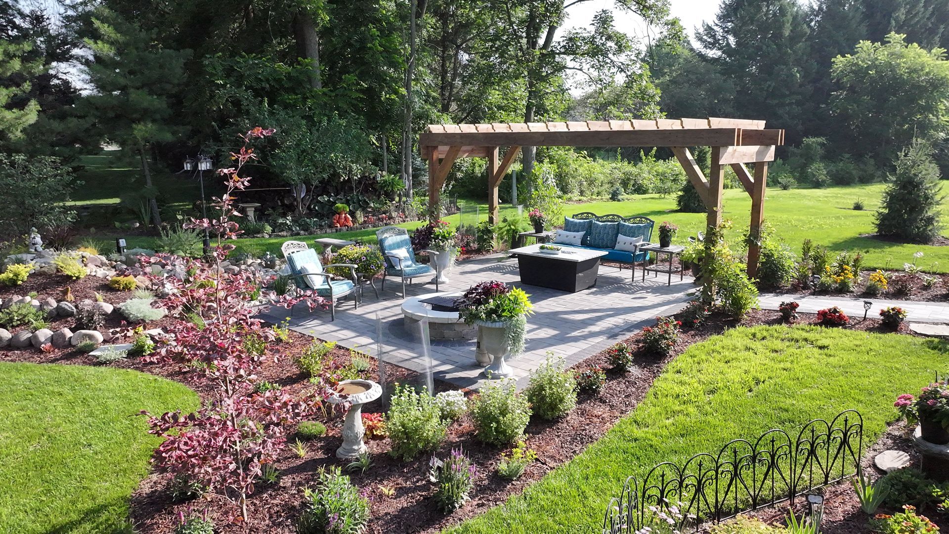 Patio with pergola, seating, fire pit, and landscaping in a backyard.