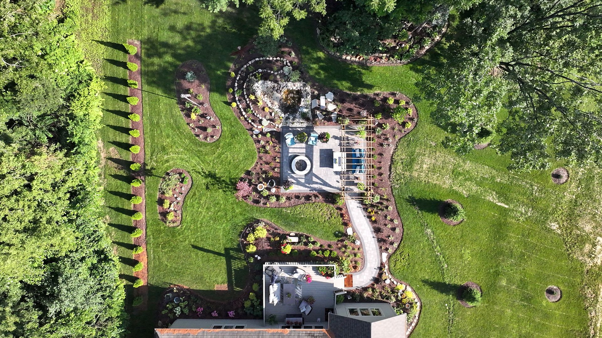 Aerial view of a landscaped backyard with gardens, a pathway, patio, and trees.