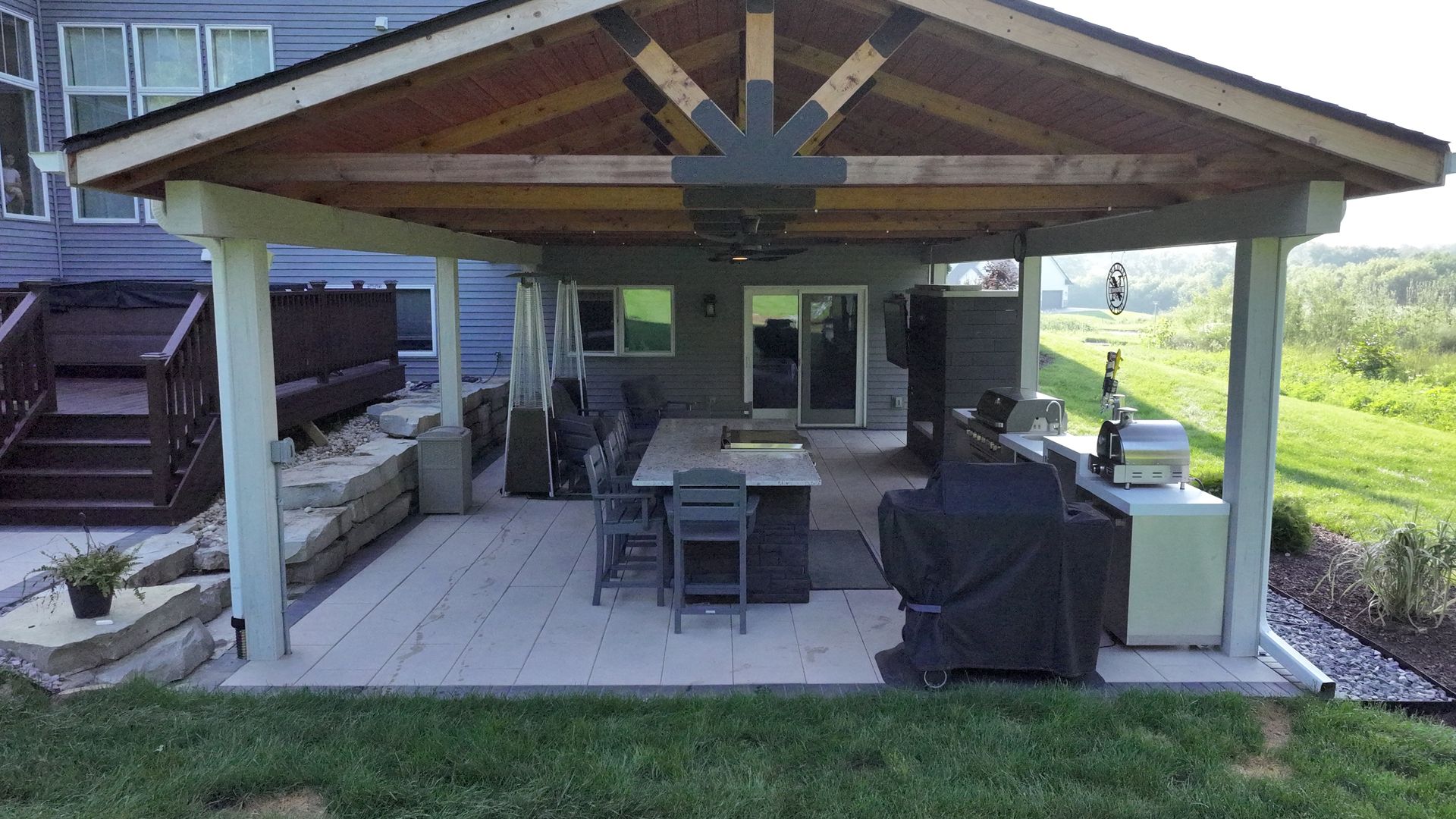 Covered patio with dining table and grill, attached to a house, in a grassy backyard.