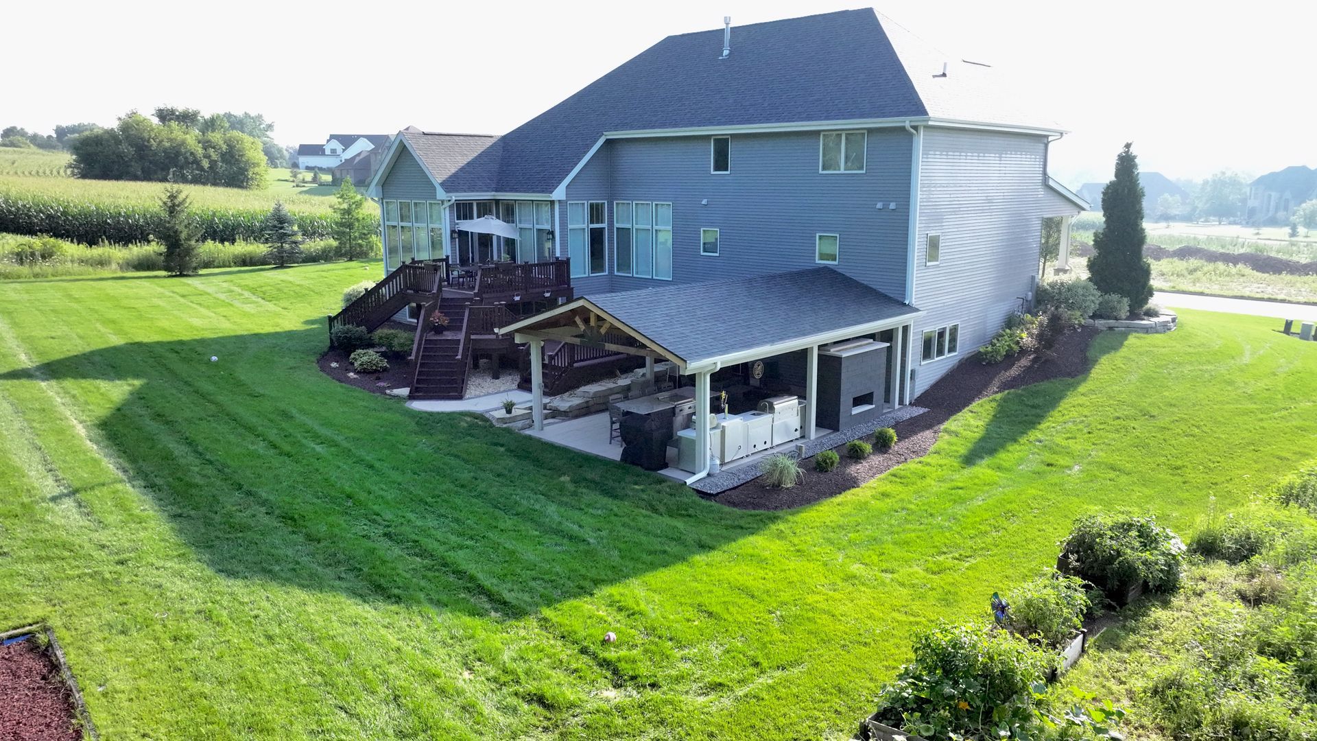Large blue house with green lawn, deck, and covered patio on a sunny day.
