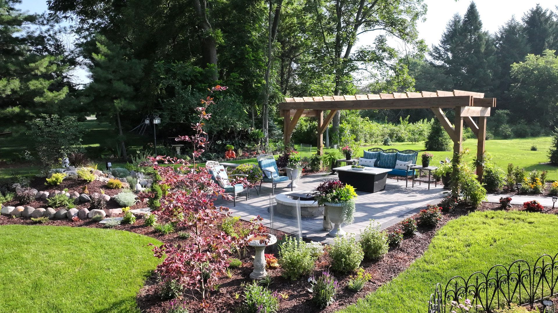 Patio with pergola, seating, fire pit, surrounded by lush landscaping and trees.