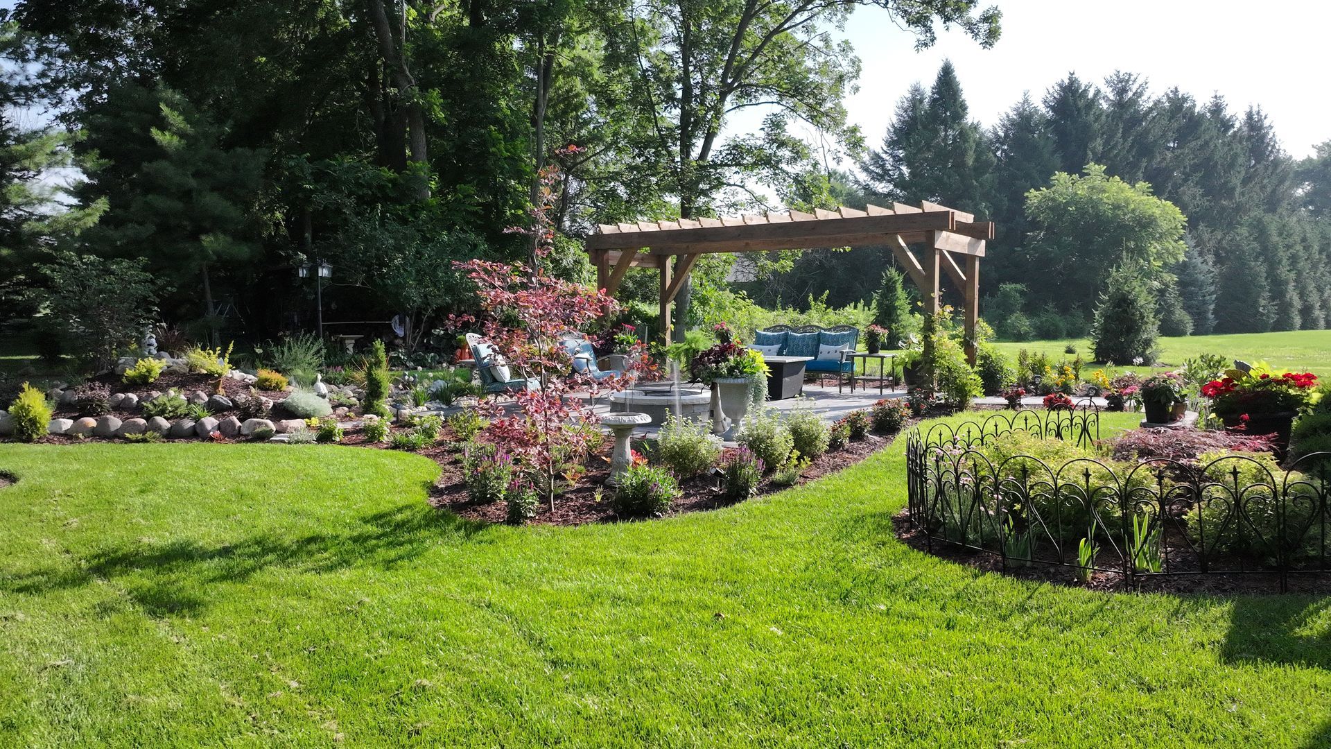 A landscaped backyard with a pergola, flower beds, and lush green lawn.