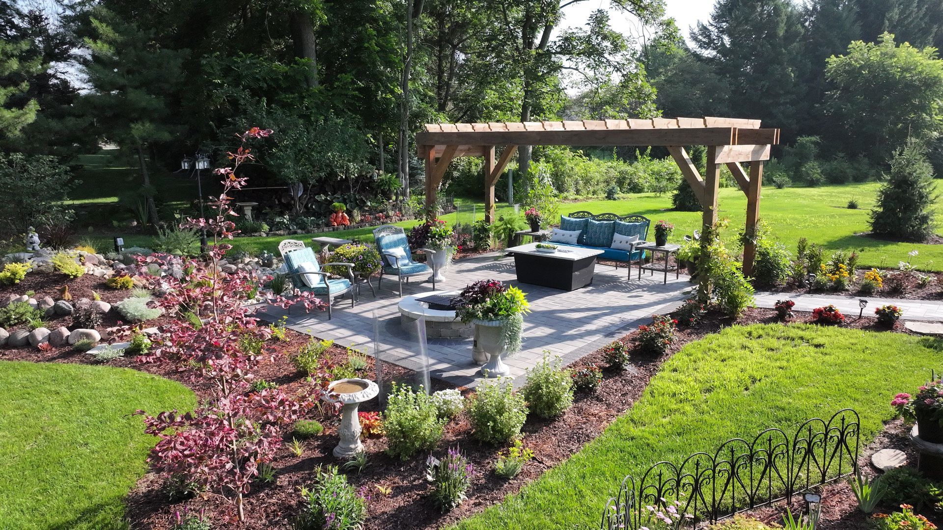Patio with pergola, seating, and flower beds in a lush green garden.