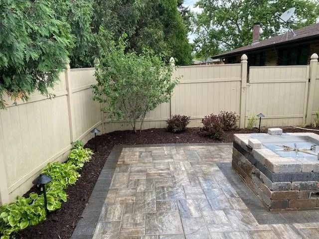 Backyard patio with a beige fence, a paved floor, and a fire pit.