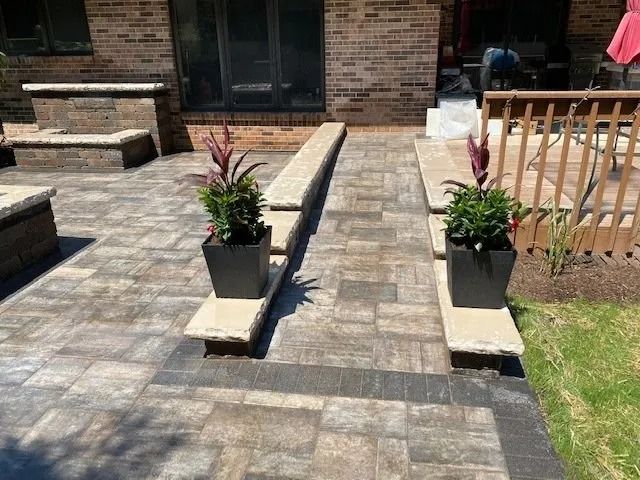 A brick patio with stone benches and planters, leading to a wooden deck.