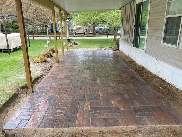 Newly constructed outdoor patio with stamped brick pattern. Brown and gray tones, partially covered by a porch.