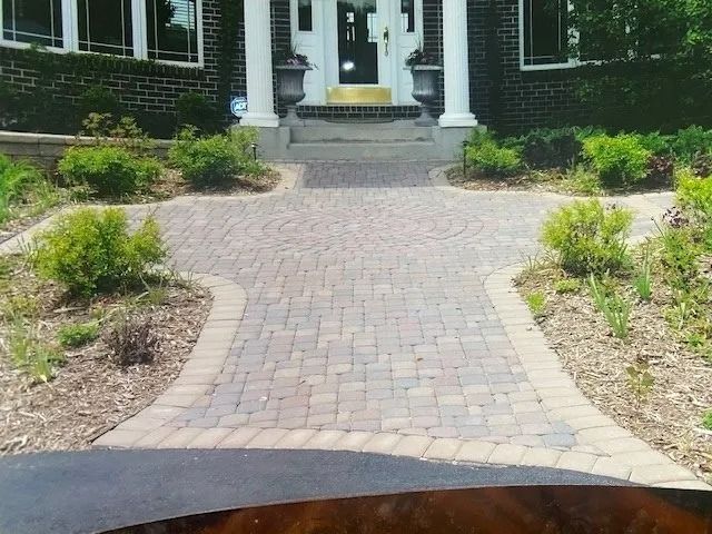 Brick walkway leading to a house's white columns and front door, flanked by landscaping and bushes.