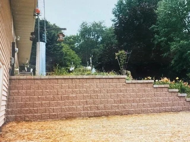 Brown retaining wall with steps, next to a building, with trees in the background.