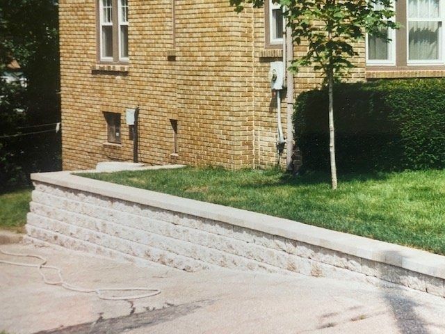 Brick building next to a white-stone retaining wall and grassy lawn.