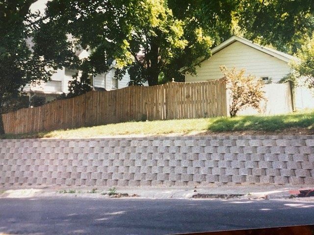 A retaining wall with a wooden fence and a house behind it.