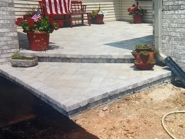 A paved patio with brick steps, flower pots, and a bench.