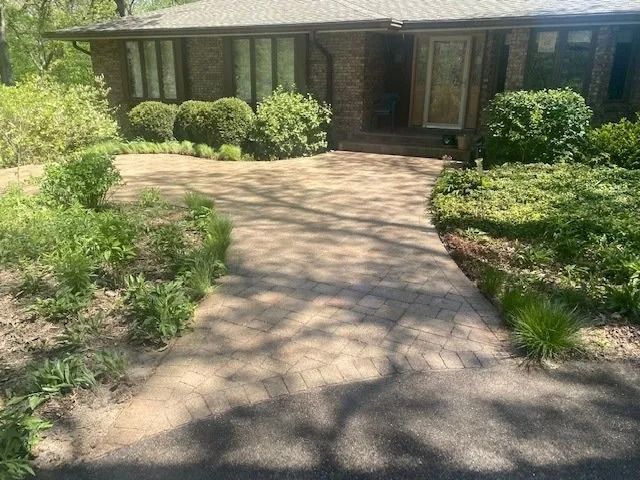 A brick house with a brick walkway and overgrown landscaping.