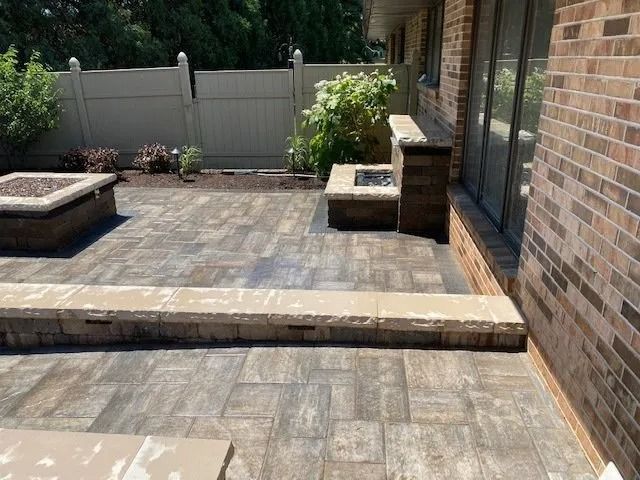 Brick patio with built-in fire pits and a low wall, next to a brick building and fence.
