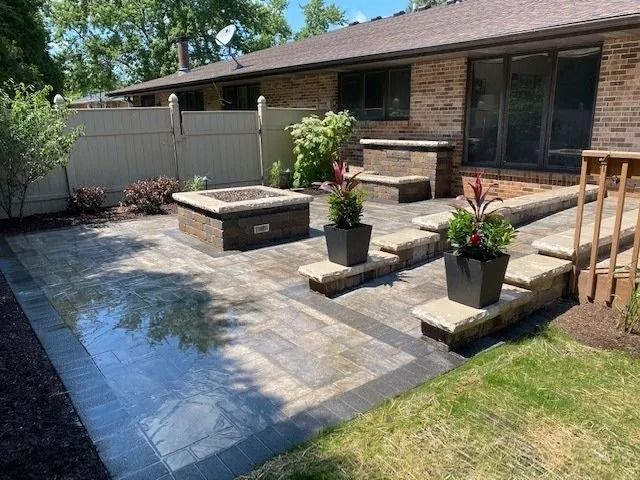 Brick patio with fire pit, retaining wall, and potted plants in a backyard setting.