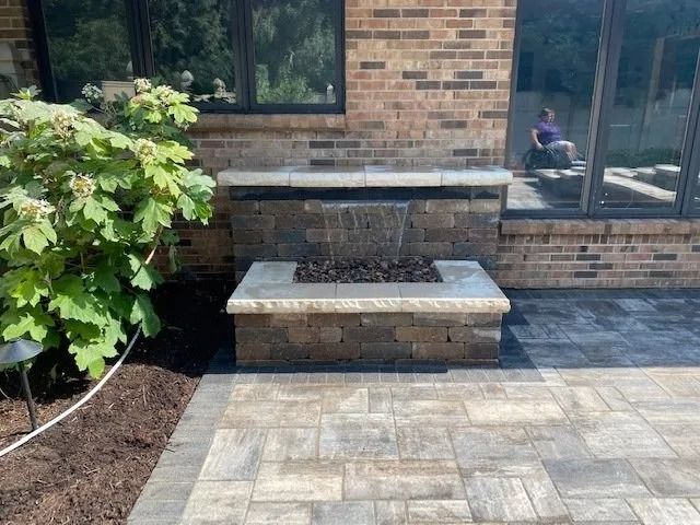 Stone patio with waterfall feature and fire pit against a brick building.