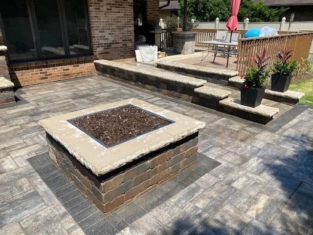 Outdoor patio with a brick fire pit and stairs leading to a deck.