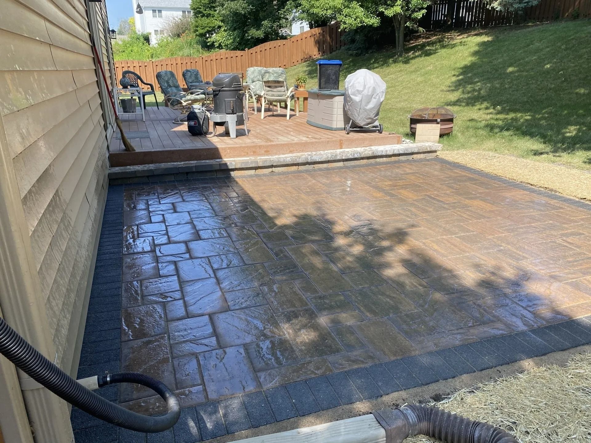 Patio with pavers and a wood deck. A hose is connected.