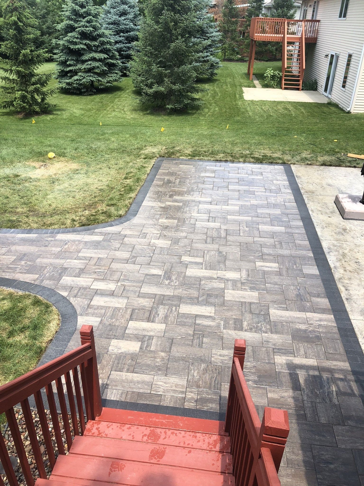 Brick patio with red stairs leading down to green grass and trees.