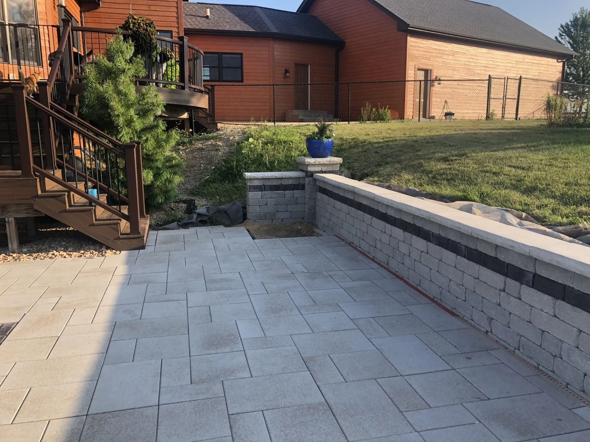 Stone patio with a retaining wall, deck, and house in the background.
